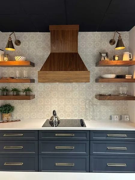 A modern kitchen featuring navy blue cabinets, a wooden range hood, open shelves with decor, and patterned wall tiles.