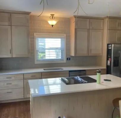A modern kitchen with light wood cabinets, white countertops, a tiled backsplash, and an island with an induction cooktop.