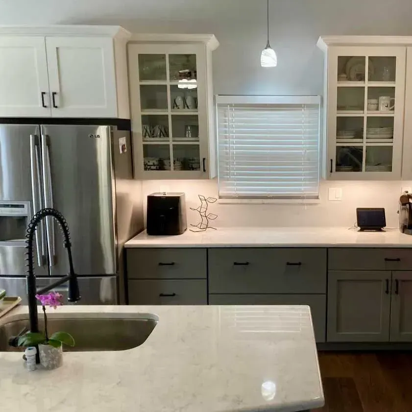 Modern kitchen with white upper cabinets, gray lower cabinets, quartz countertops, stainless appliances, and island sink.