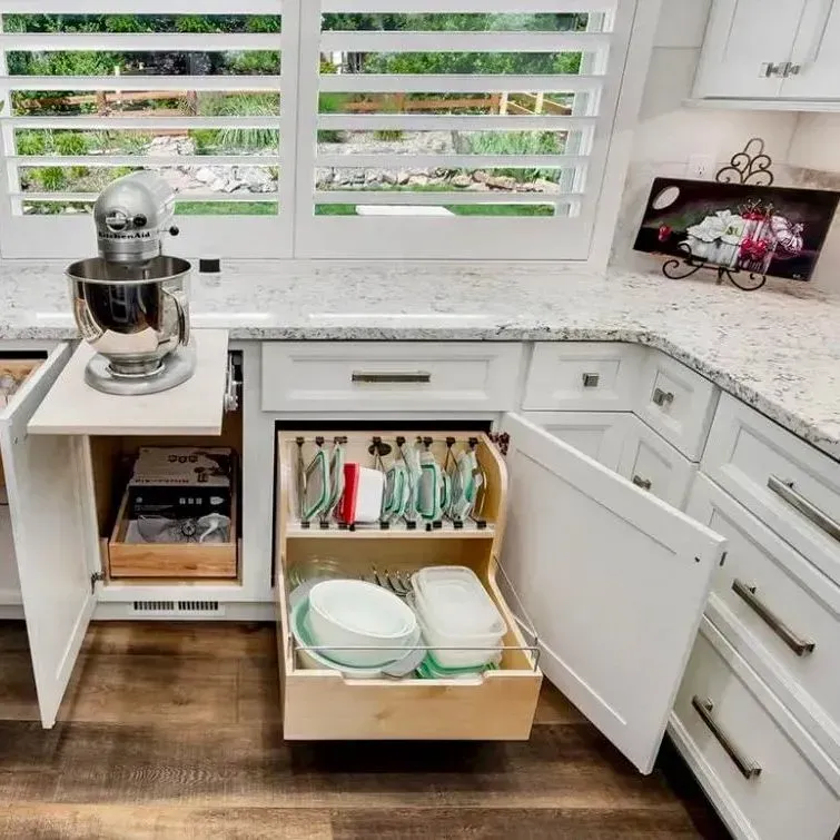 A white kitchen cabinet with an open pull-out stand for a mixer and a lower drawer organized with bowls and storage lids.