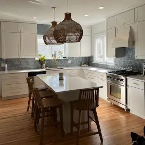 A bright kitchen with white cabinets, light wood floors, a center island with bar stools, and dark woven pendant lights.