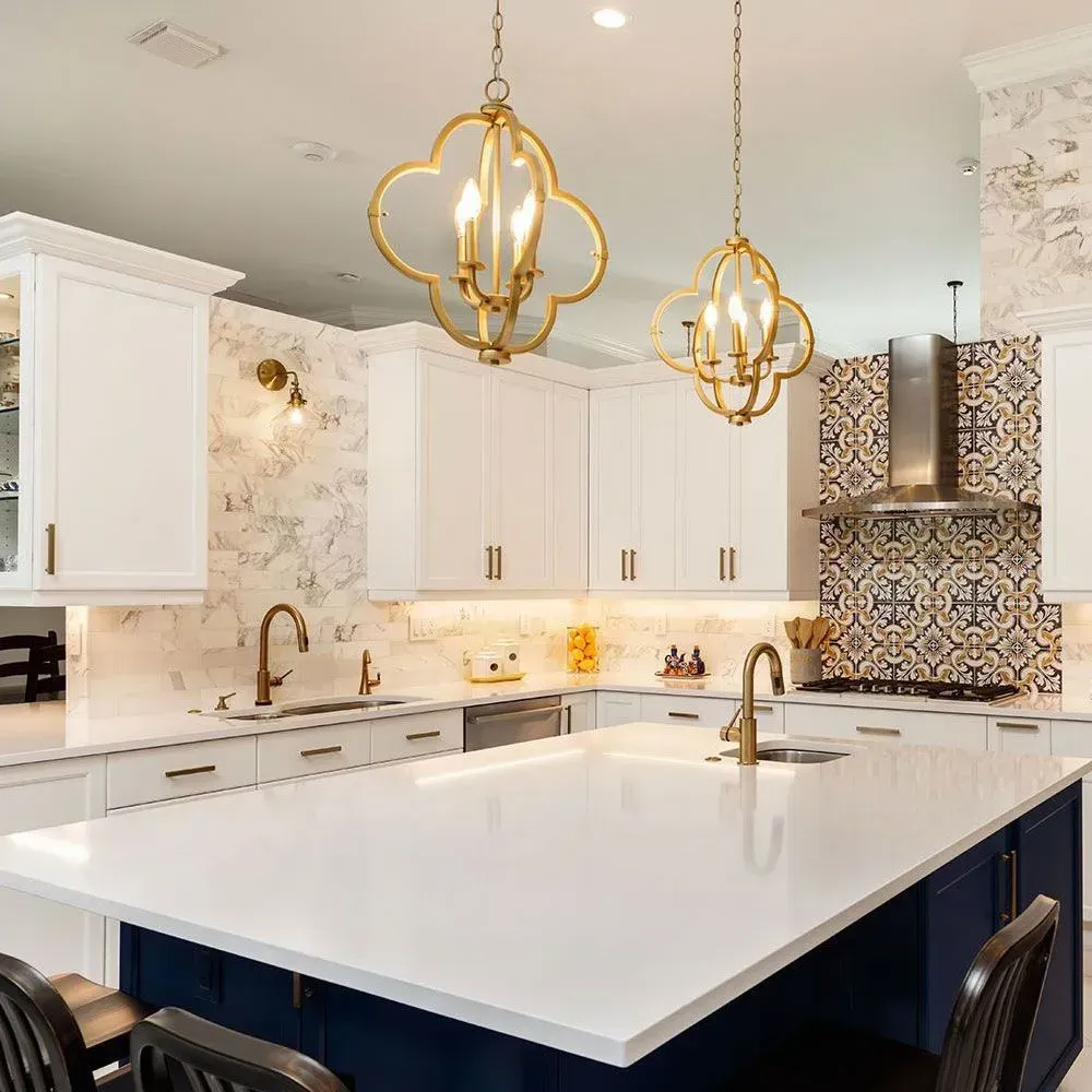 A modern kitchen with white cabinetry, a large white island with blue base, patterned backsplash, and two gold pendants.