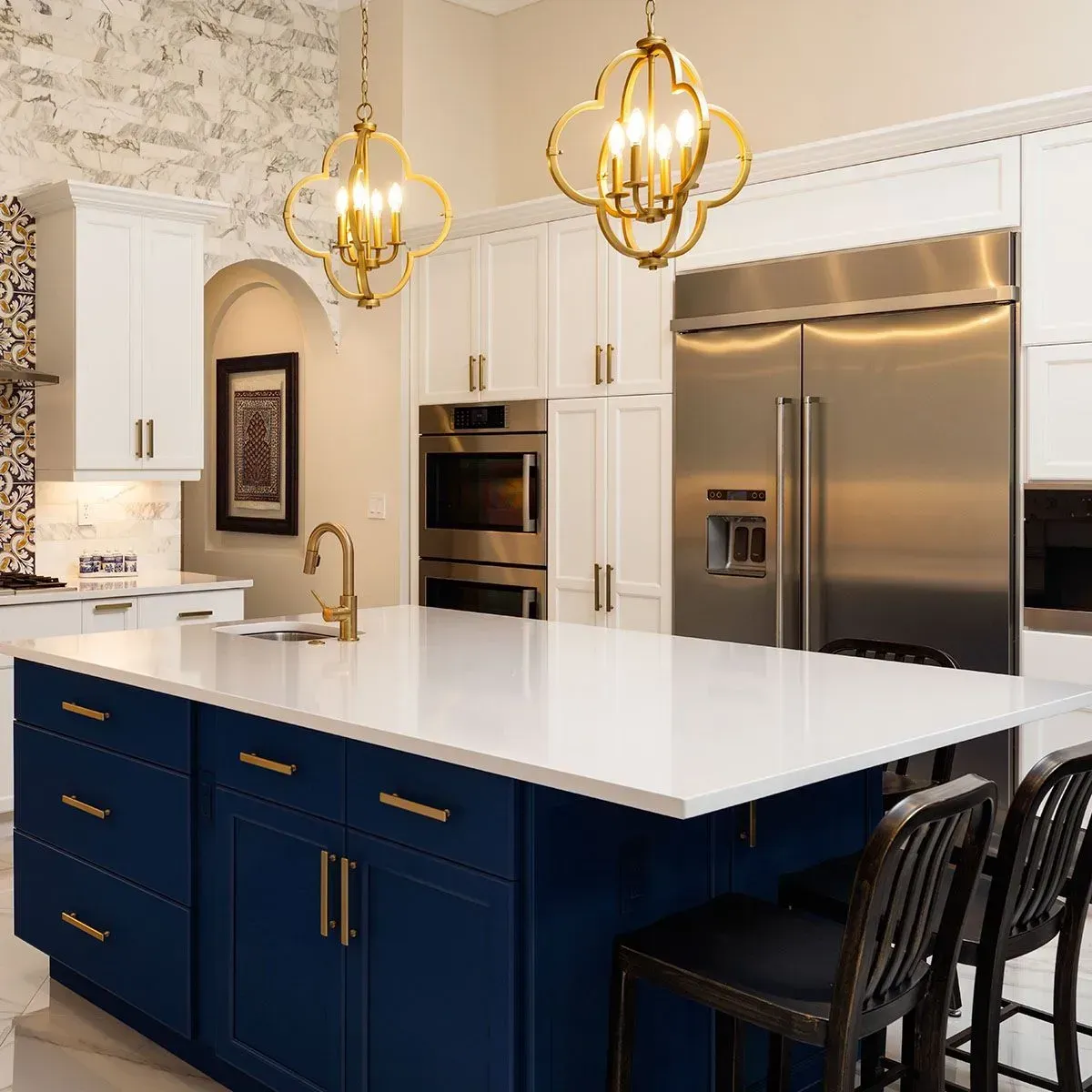 A kitchen island with navy cabinets and a white countertop, featuring gold pendant lights and stainless steel appliances.