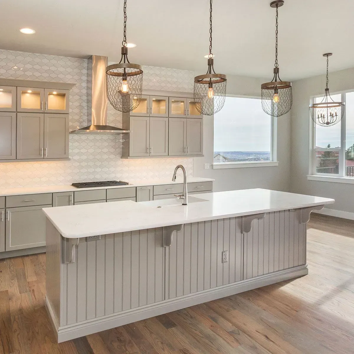 A modern kitchen features a large white island, gray cabinets, stainless appliances, and three hanging wire pendant lights.