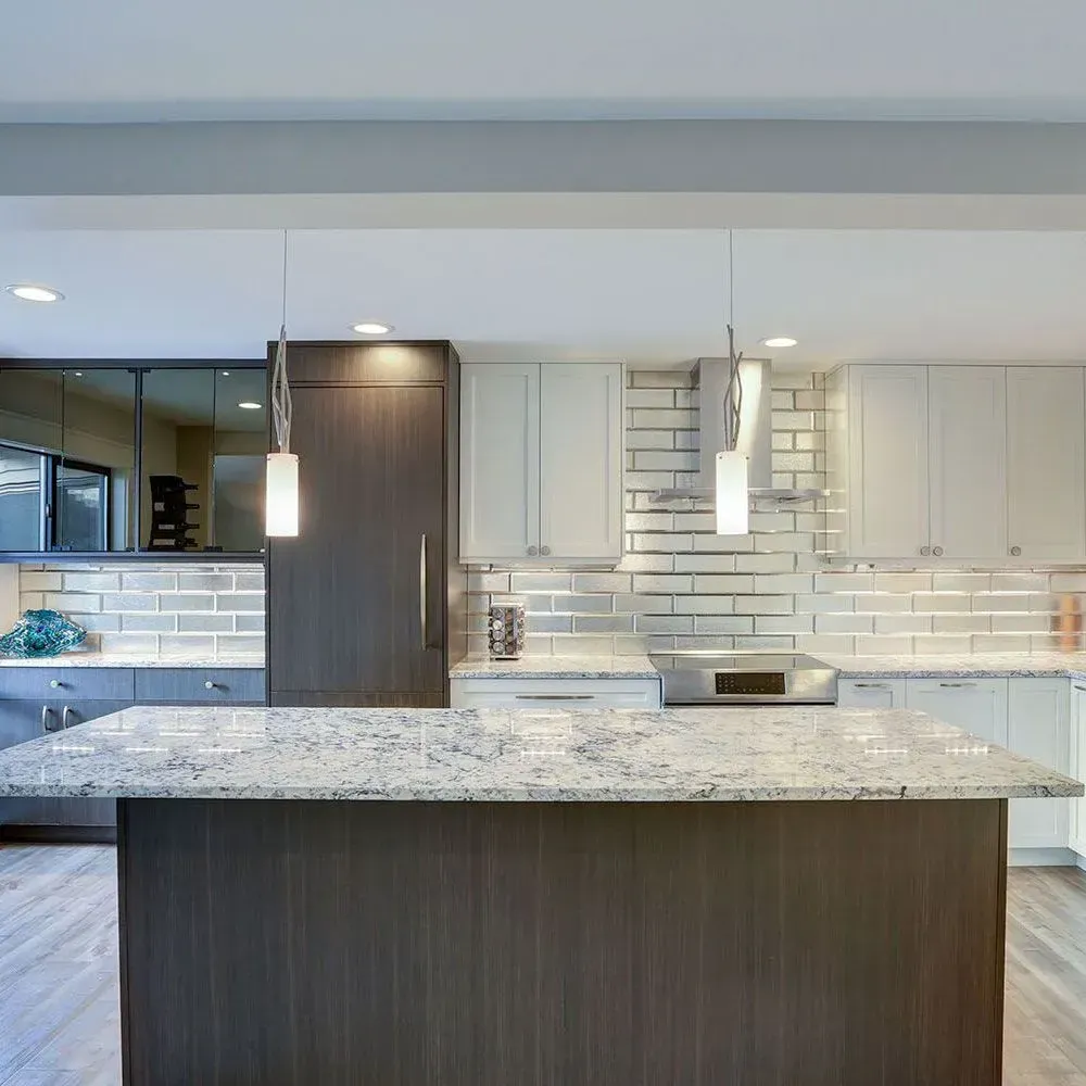 Modern kitchen with a white granite island, dark wood cabinetry, white subway tile backsplash, and two hanging pendants.