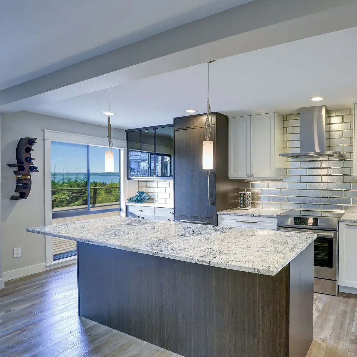 Modern kitchen with a dark wood island, granite countertops, white cabinets, and a scenic water view through large windows.