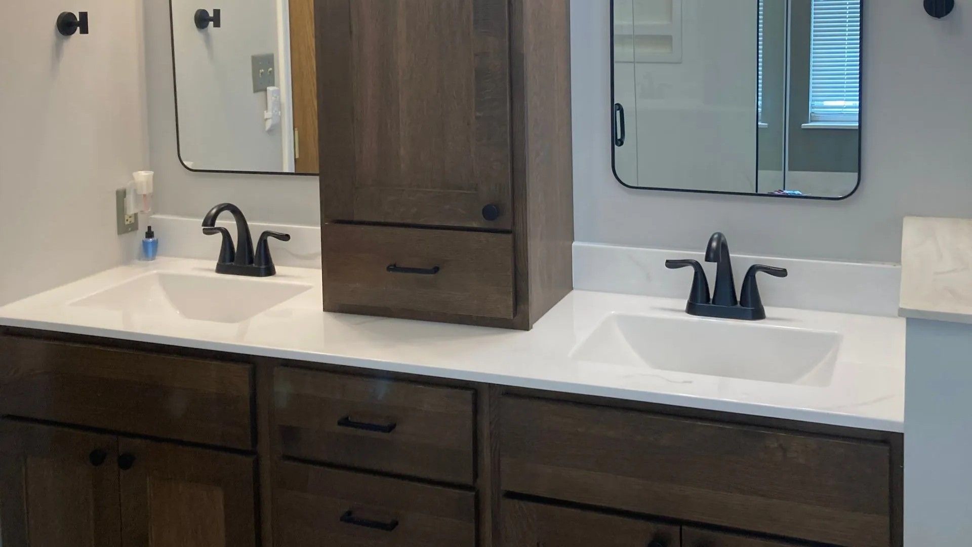 A double bathroom vanity with dark wood cabinets, white countertops, two sinks, black faucets, and matching mirrors.