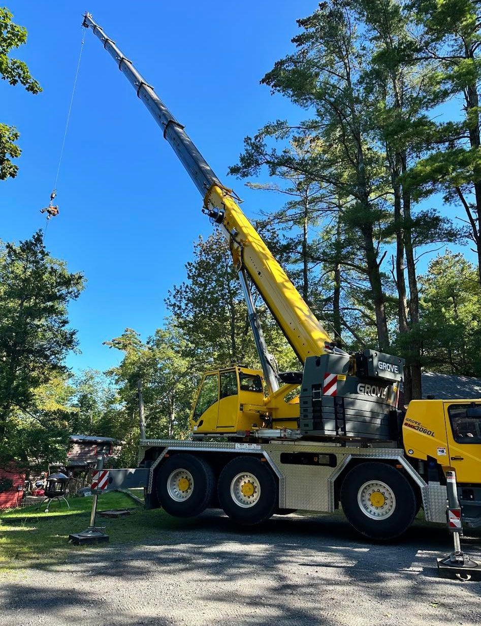 A large yellow crane is parked in a gravel lot with trees in the background.