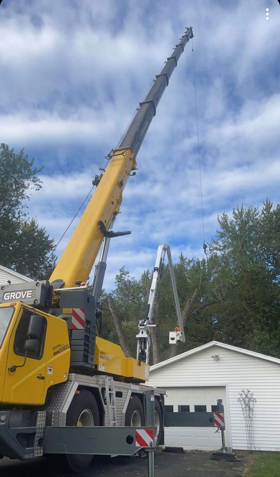 A large yellow crane is sitting in front of a white house.