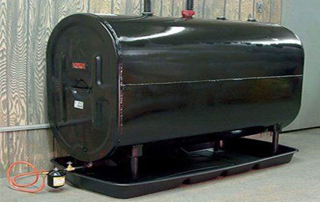 A black, horizontal cylindrical oil tank sits on a black spill containment tray against a wood-paneled wall.