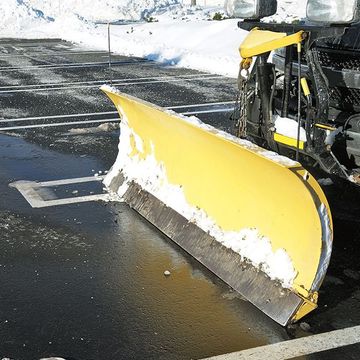 A yellow snow plow is parked in a parking lot