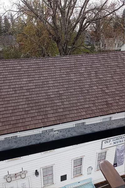 A white building with a brown roof and a tree in the background.