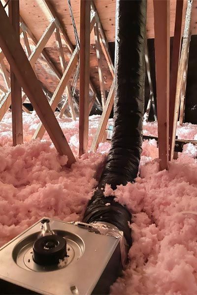 A close up of a duct in an attic filled with pink insulation.