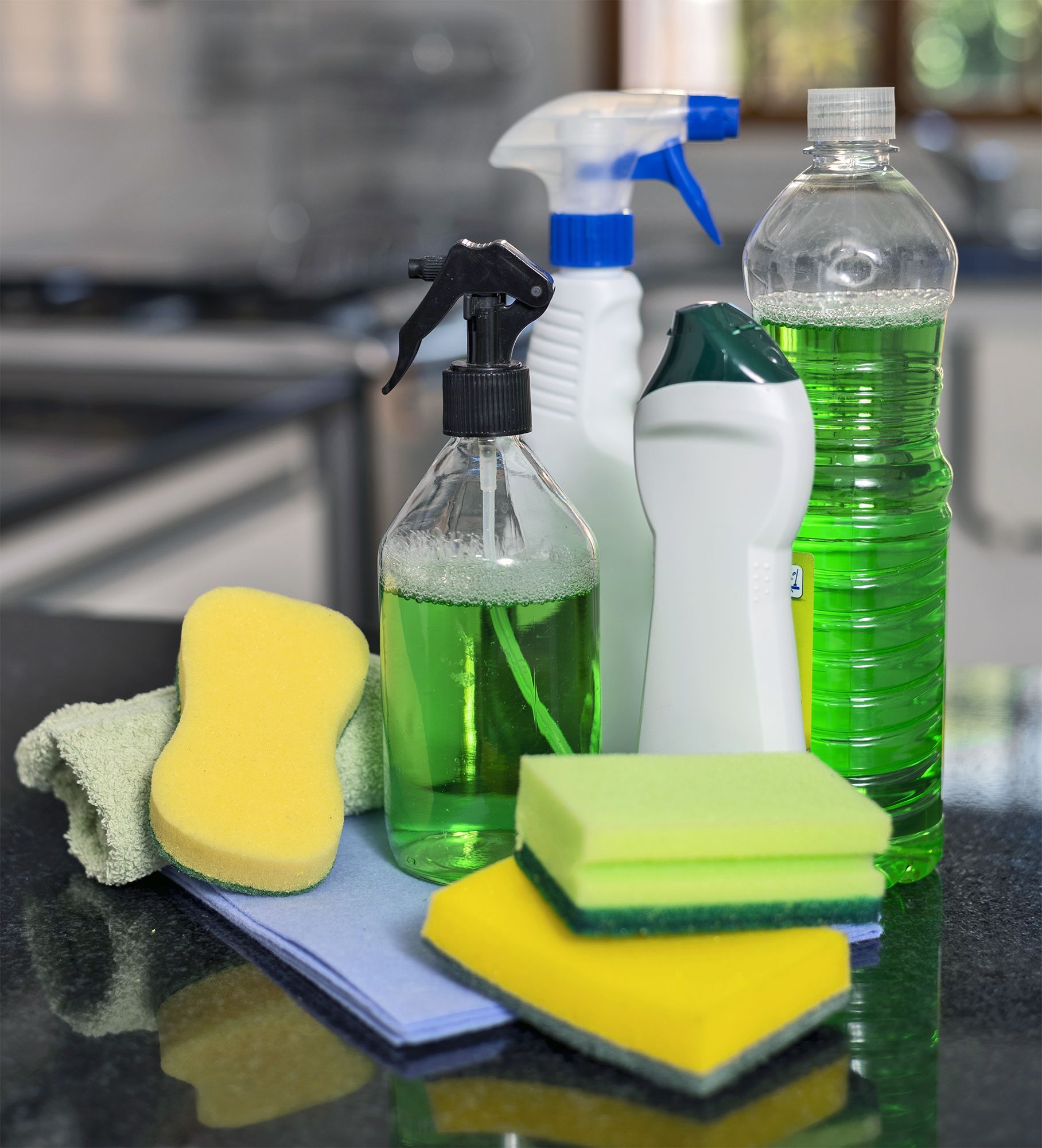 Cleaning supplies: bottles of liquid, spray bottles, sponges, and a cloth on a countertop.
