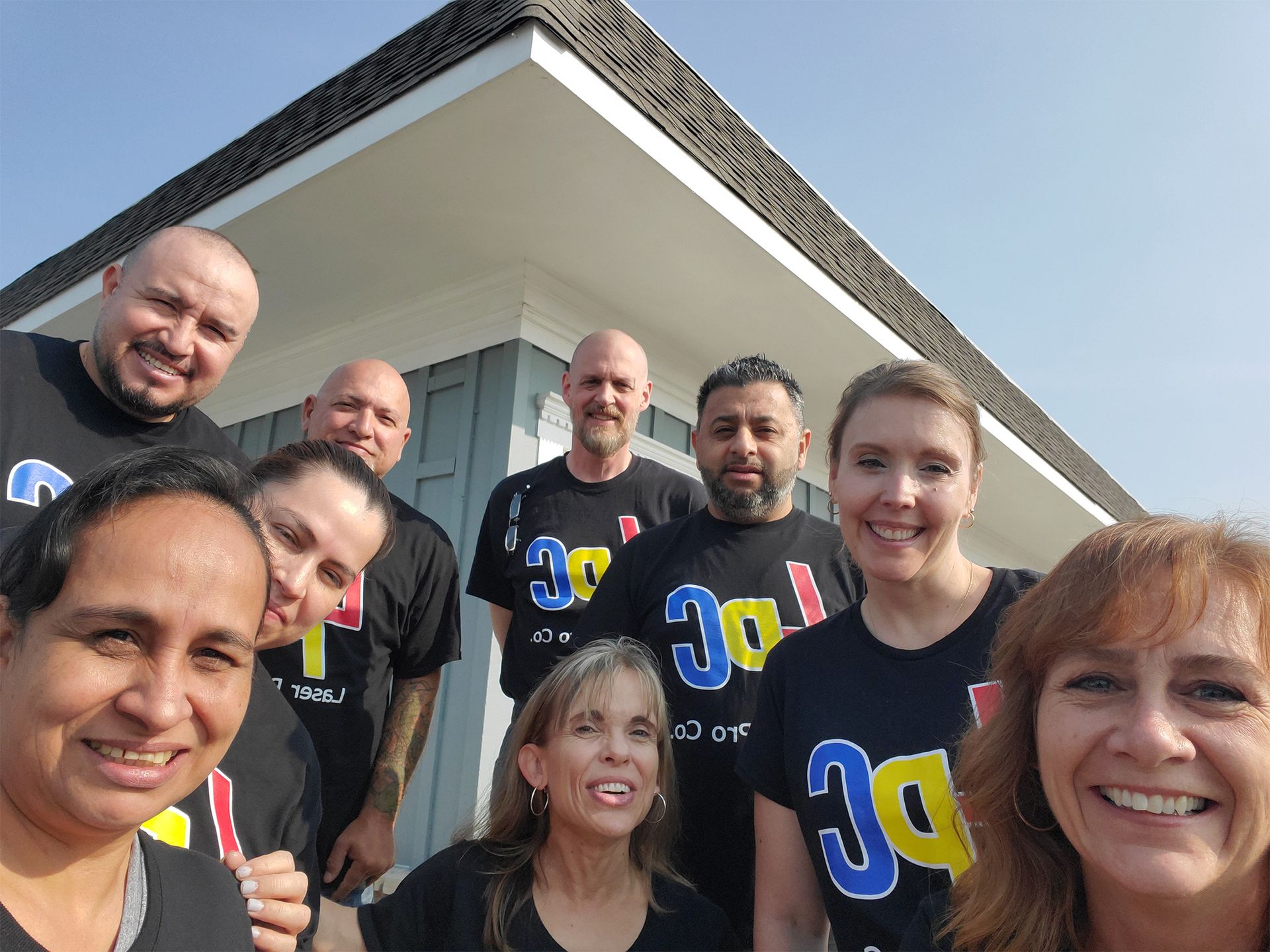 Group of people in black shirts with colorful logo, smiling in front of a building.