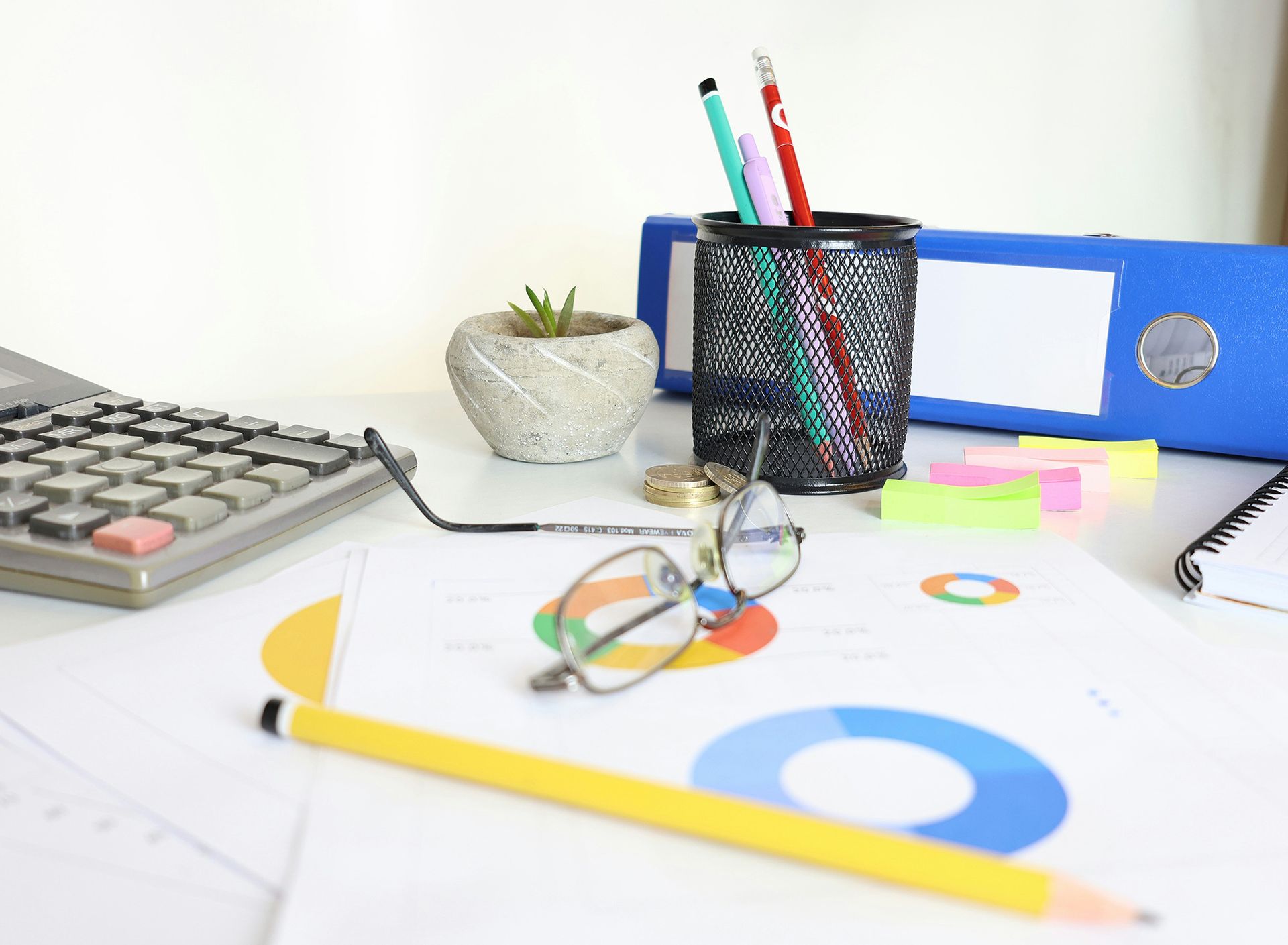 Desk with financial documents, calculator, pencils, glasses, and a binder.