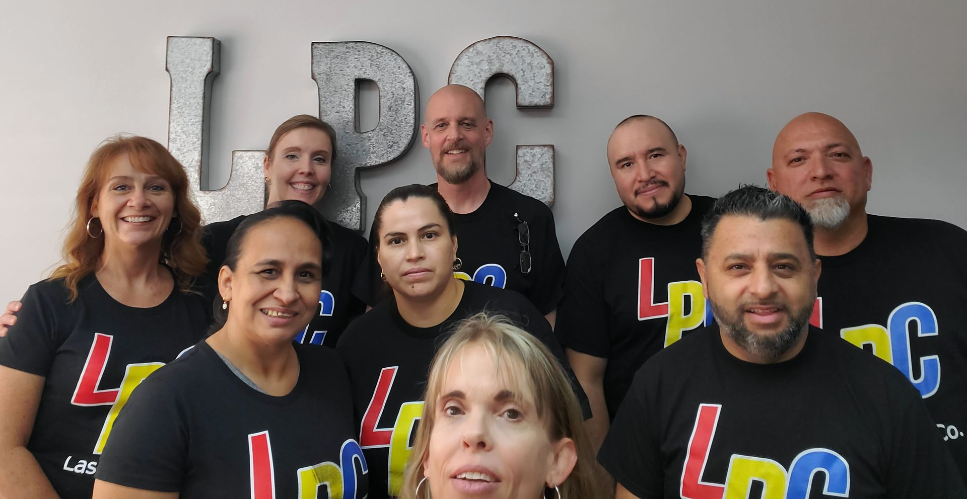 Group of nine people in black LPC logo shirts pose in front of LPC letters.