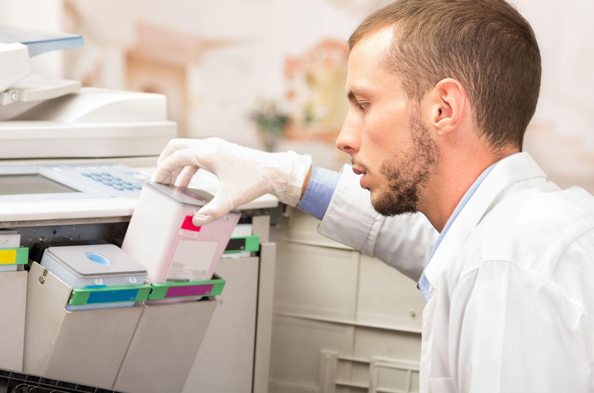 Person in lab coat replacing a pink ink cartridge in a printer.