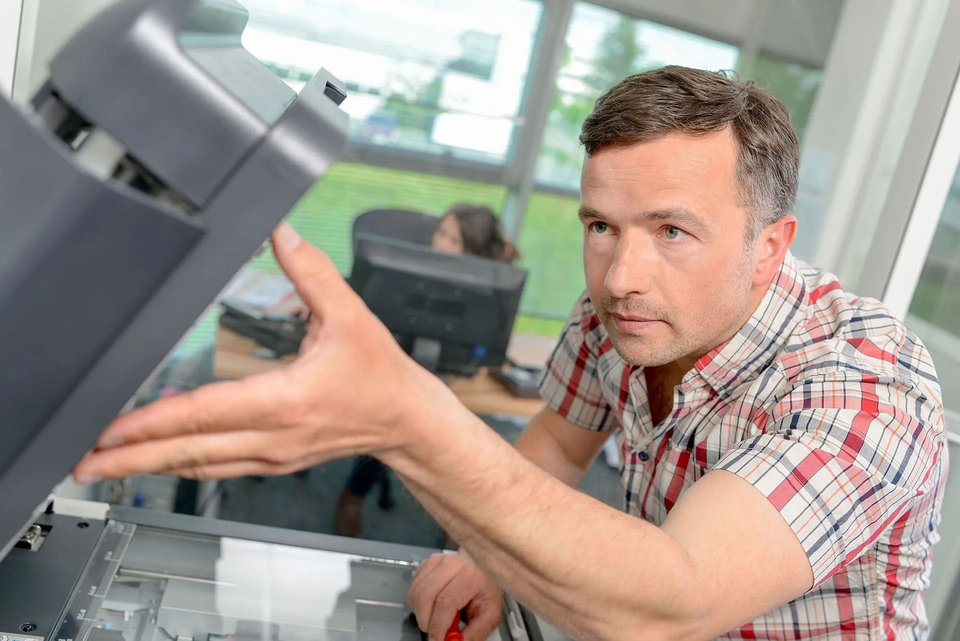 Man in plaid shirt examines a copier in an office.