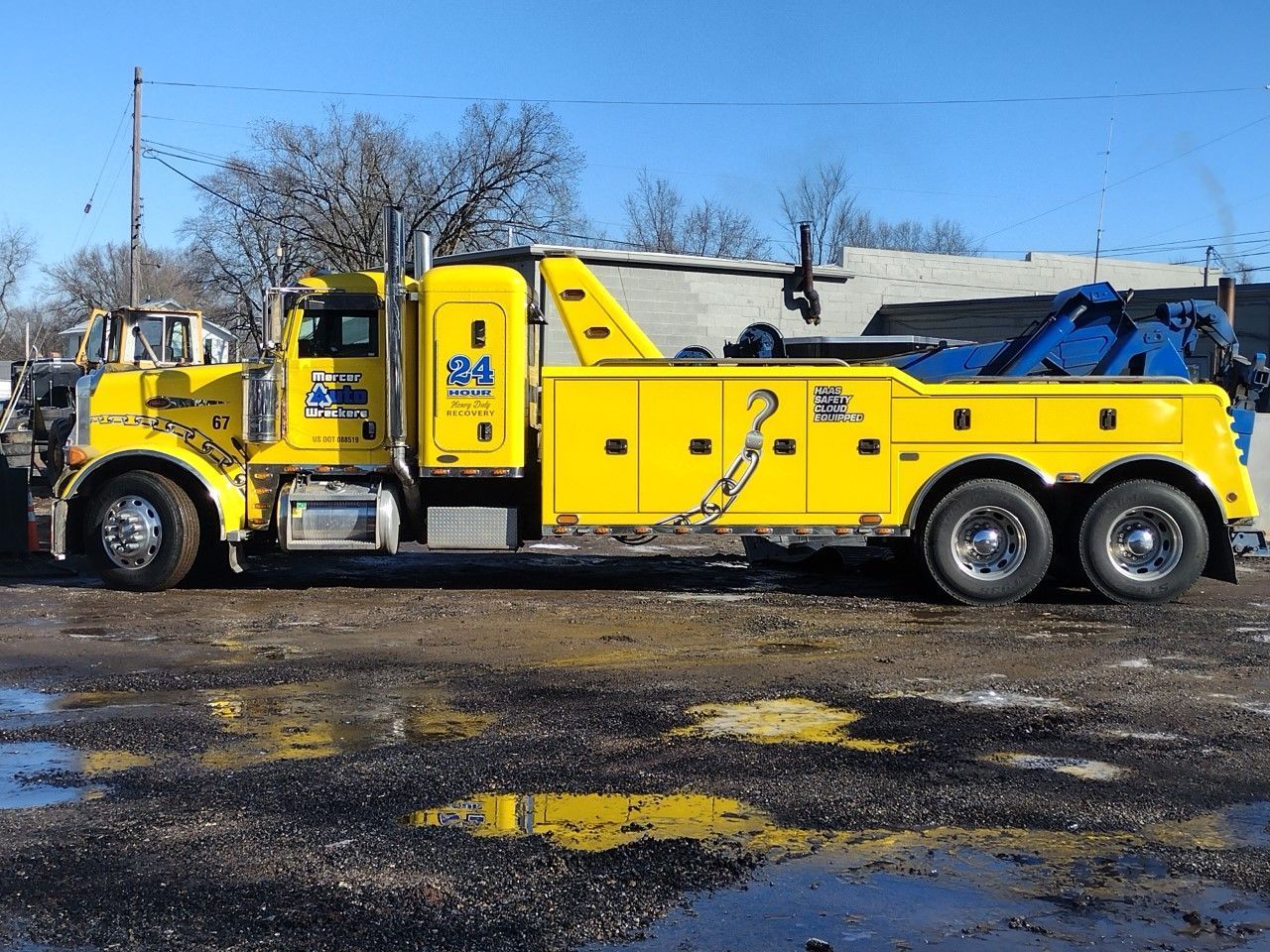 Yellow tow truck parked on a wet lot under a clear blue sky