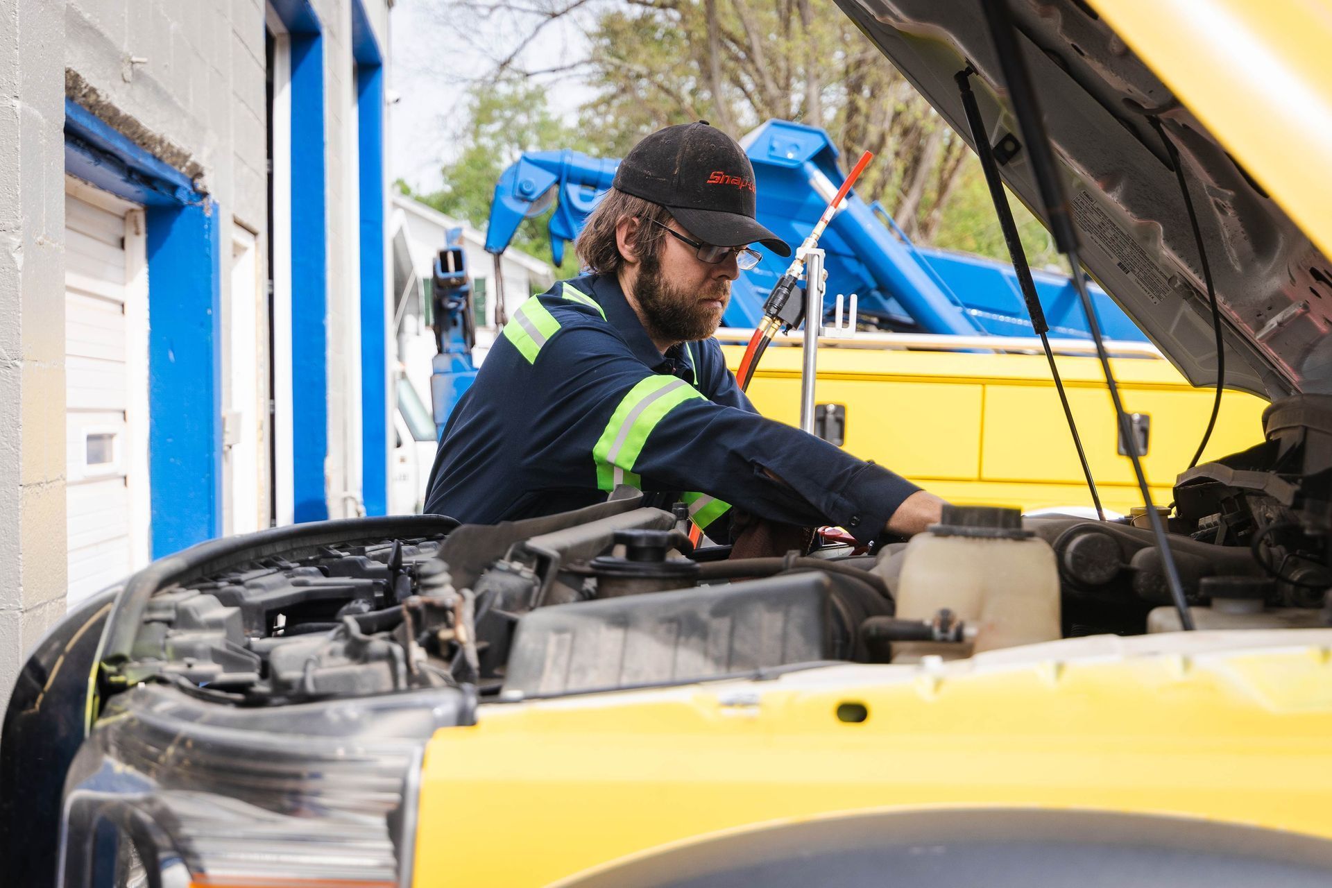 Mechanic inspecting a yellow car with the hood open in a garage