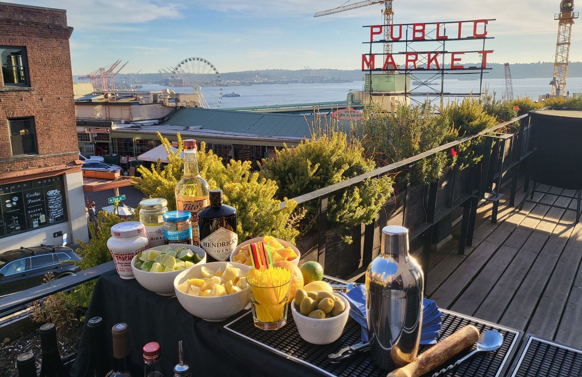A rooftop view of Pike Place Market in Seattle with a bar setup, cocktail shaker, snacks, and drinks overlooking the bay.