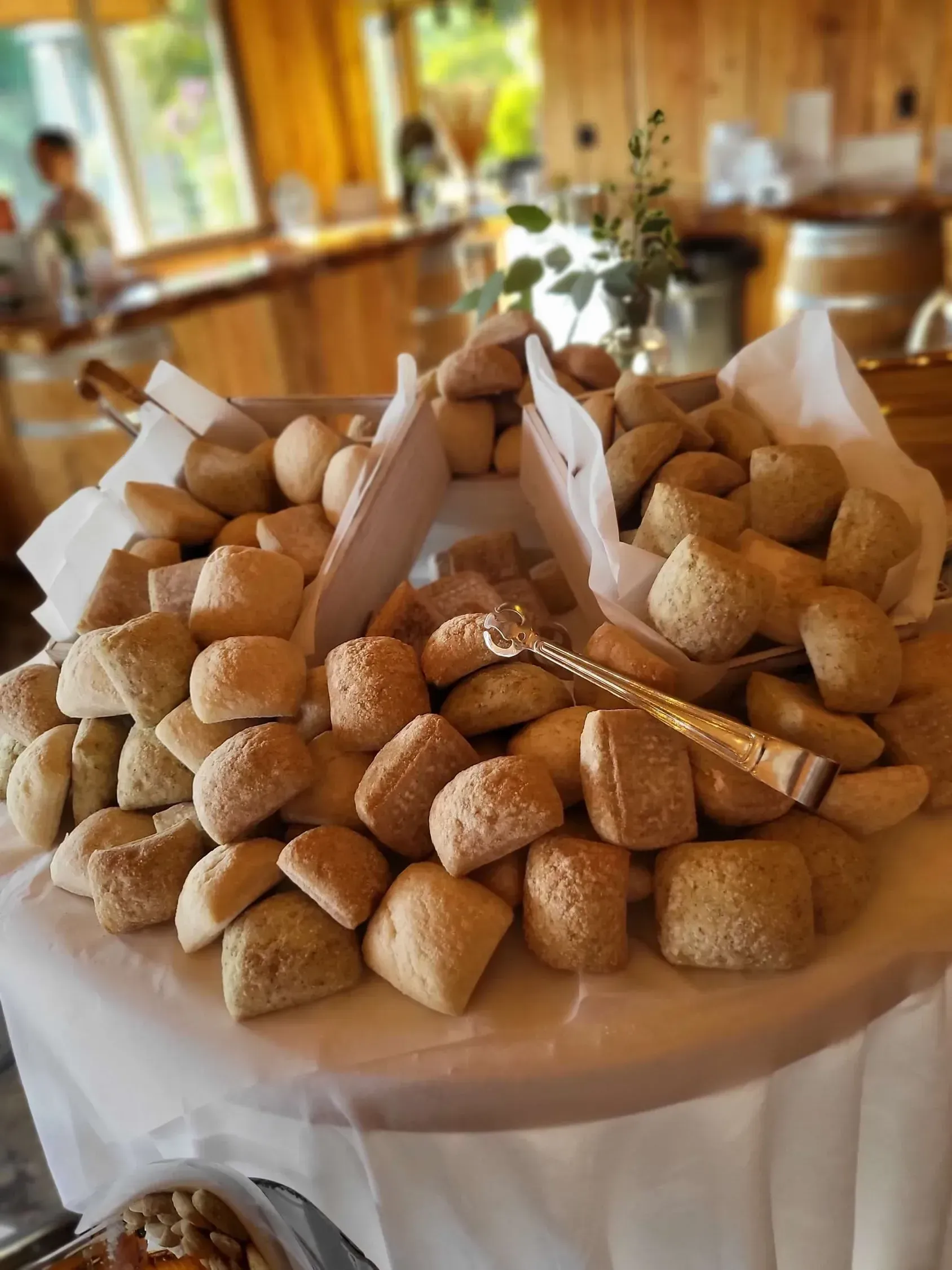 A large pile of dinner rolls served on a round platter lined with white paper, set up in a restaurant or event space.