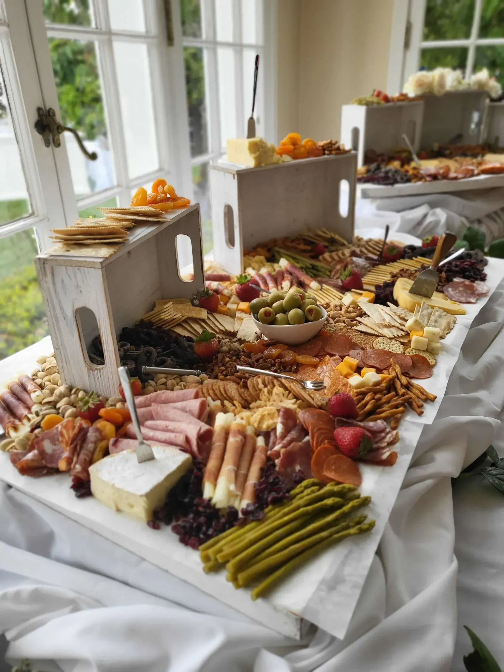 A large, lavish charcuterie board featuring cheese, meats, crackers, fruit, and asparagus, set on a white-draped table.