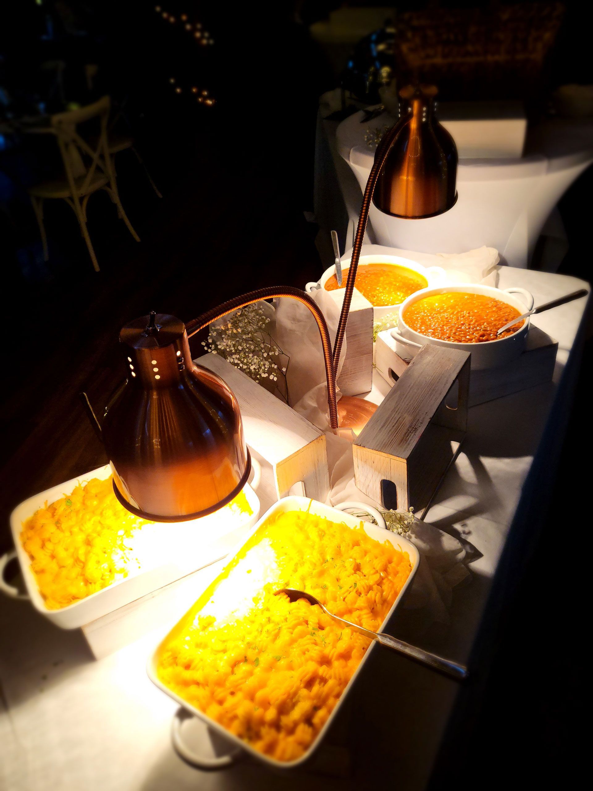Several trays of food are sitting on a table under lamps