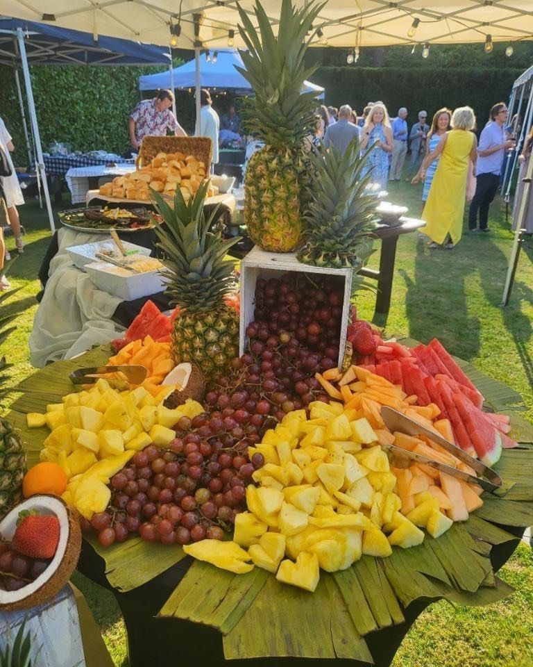 A table filled with lots of fruit including pineapples and grapes at an outdoor reception