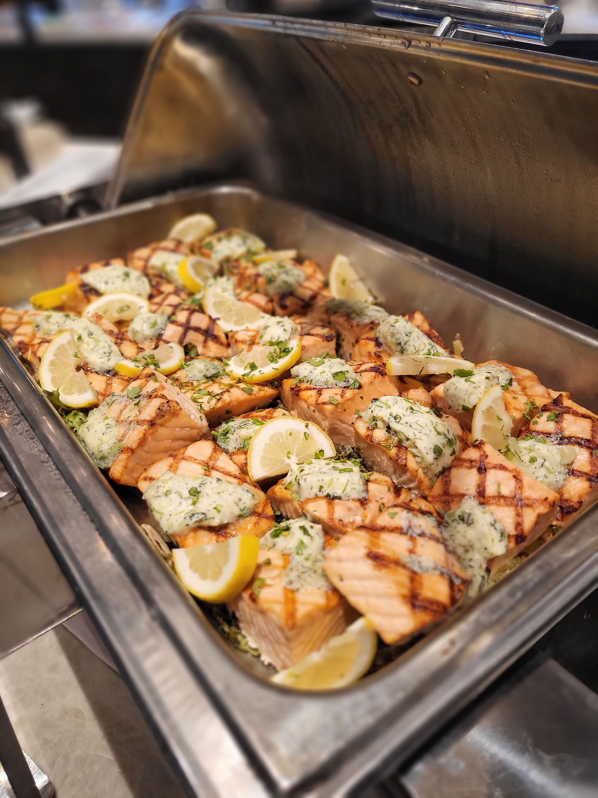 A buffet tray filled with grilled salmon and lemon slices.