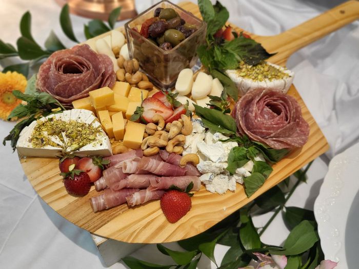 A wooden cutting board filled with meat , cheese , nuts and strawberries.