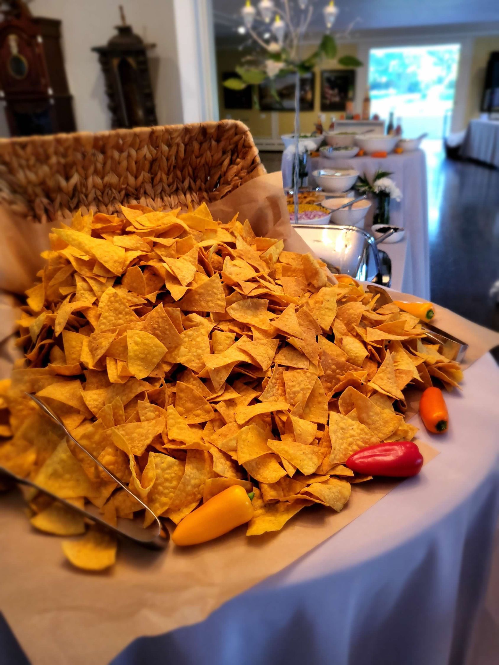 Large pile of tortilla chips on a buffet table, next to peppers and other food items.