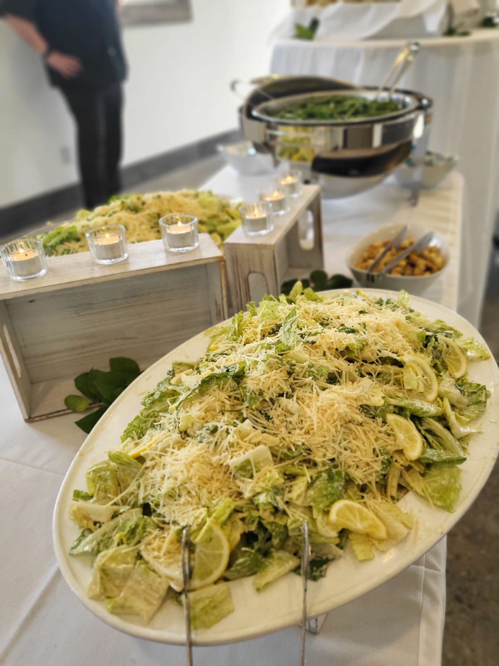 Buffet table with large platters of Caesar salad, and other dishes, with lit candles in holders.