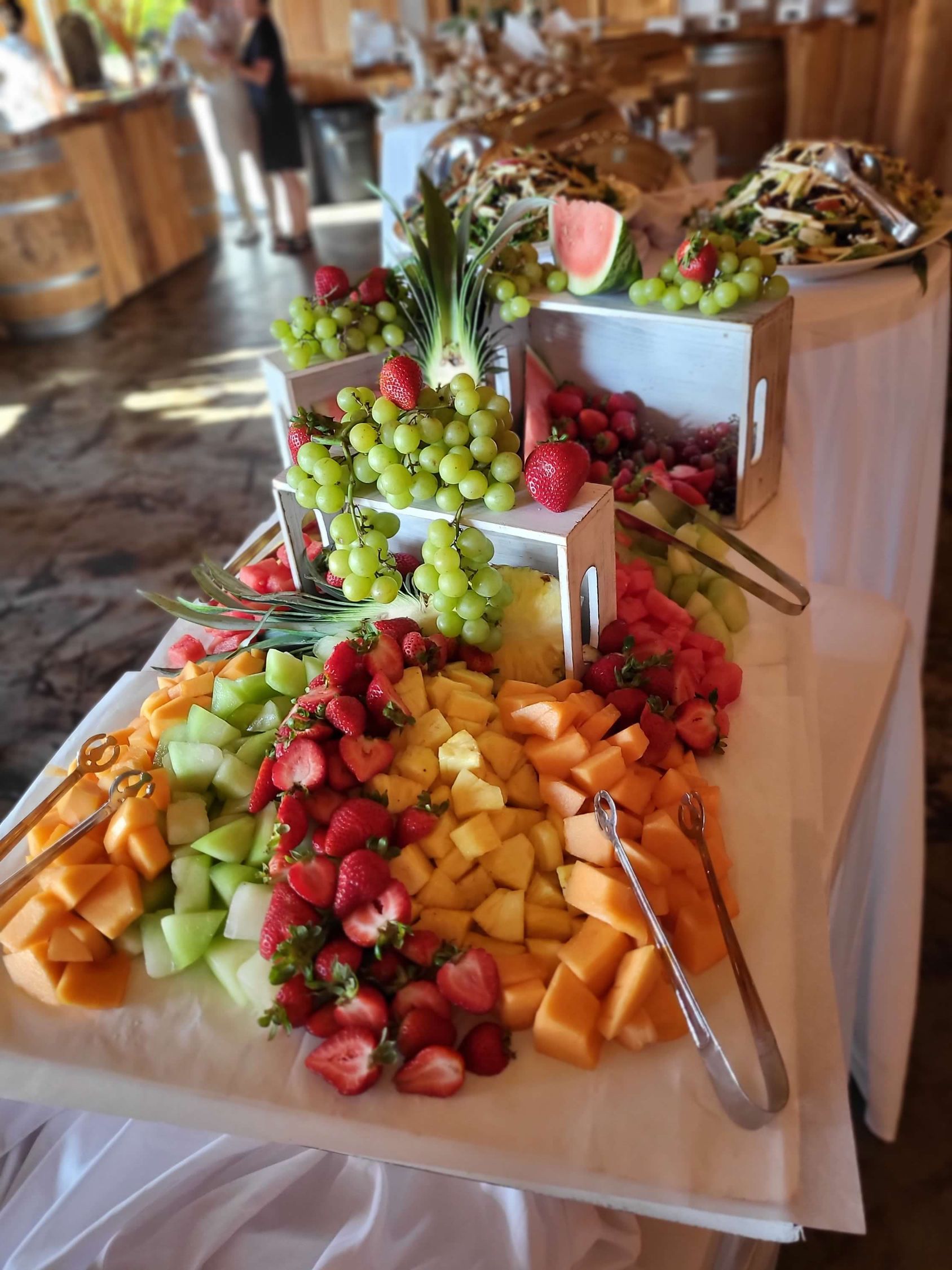 Fruit display: Grapes, strawberries, melon, and pineapple arranged on a table with tongs.