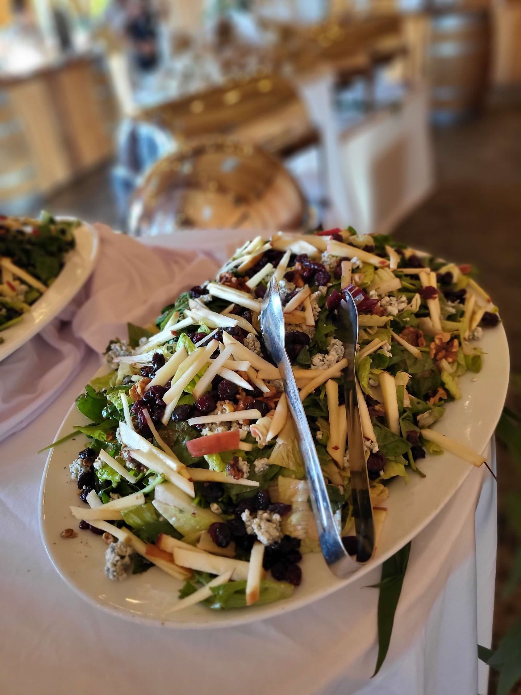 Salad platter with apples, cranberries, and nuts, served at an event, with serving tongs.