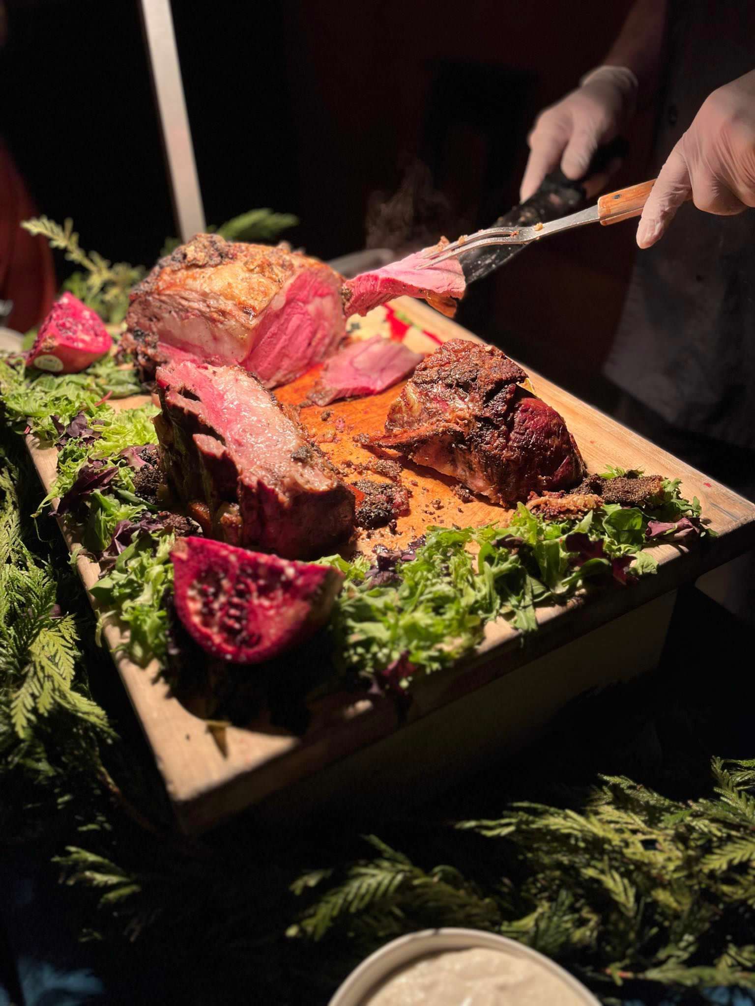 Person carving cooked meat on a wooden platter with garnish.