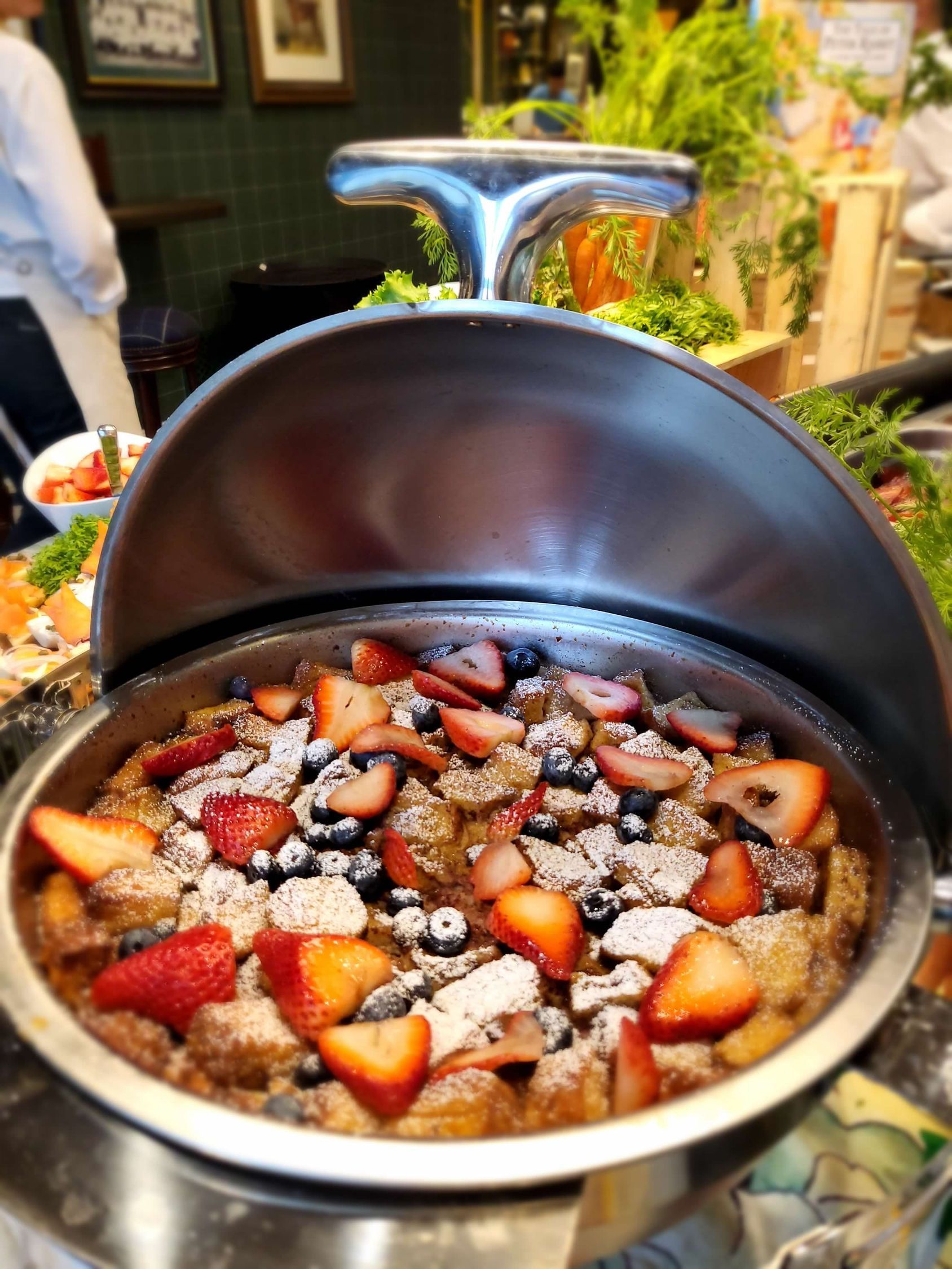 Strawberry and blueberry bread pudding in a metal chafing dish, ready to serve at a buffet.