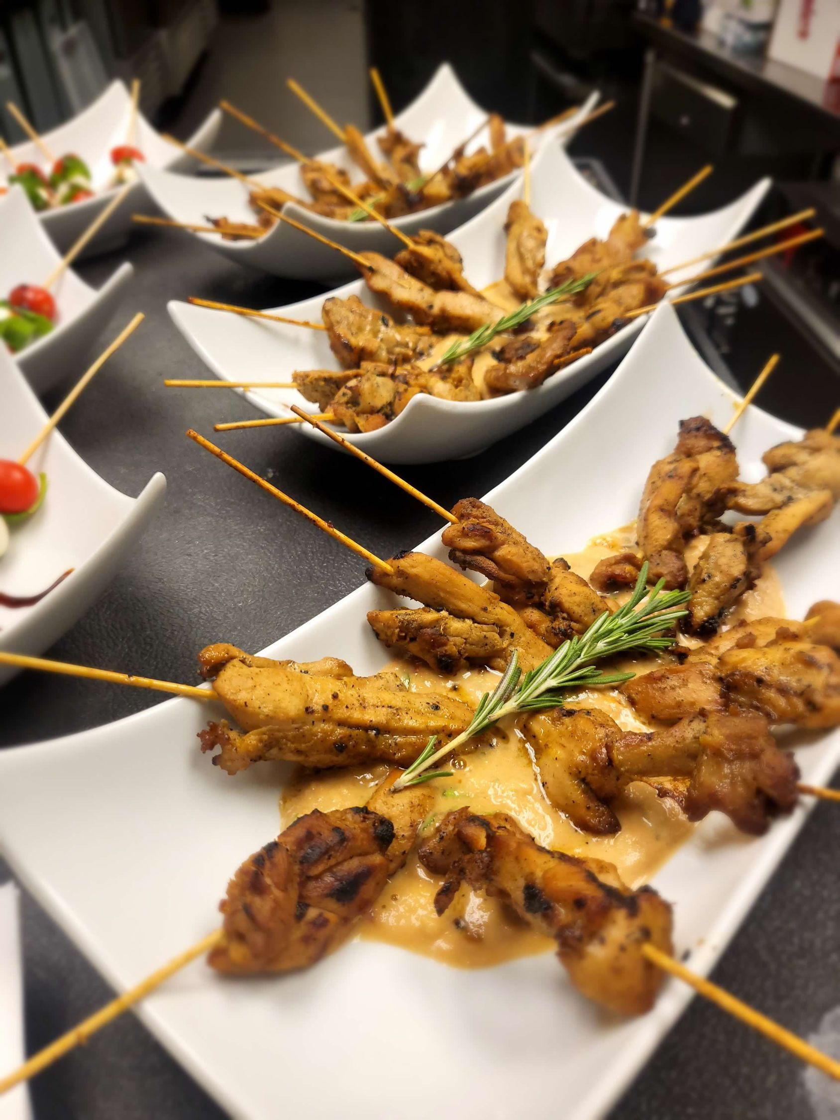 Skewered chicken appetizers on white plates, drizzled with sauce and garnished with rosemary.