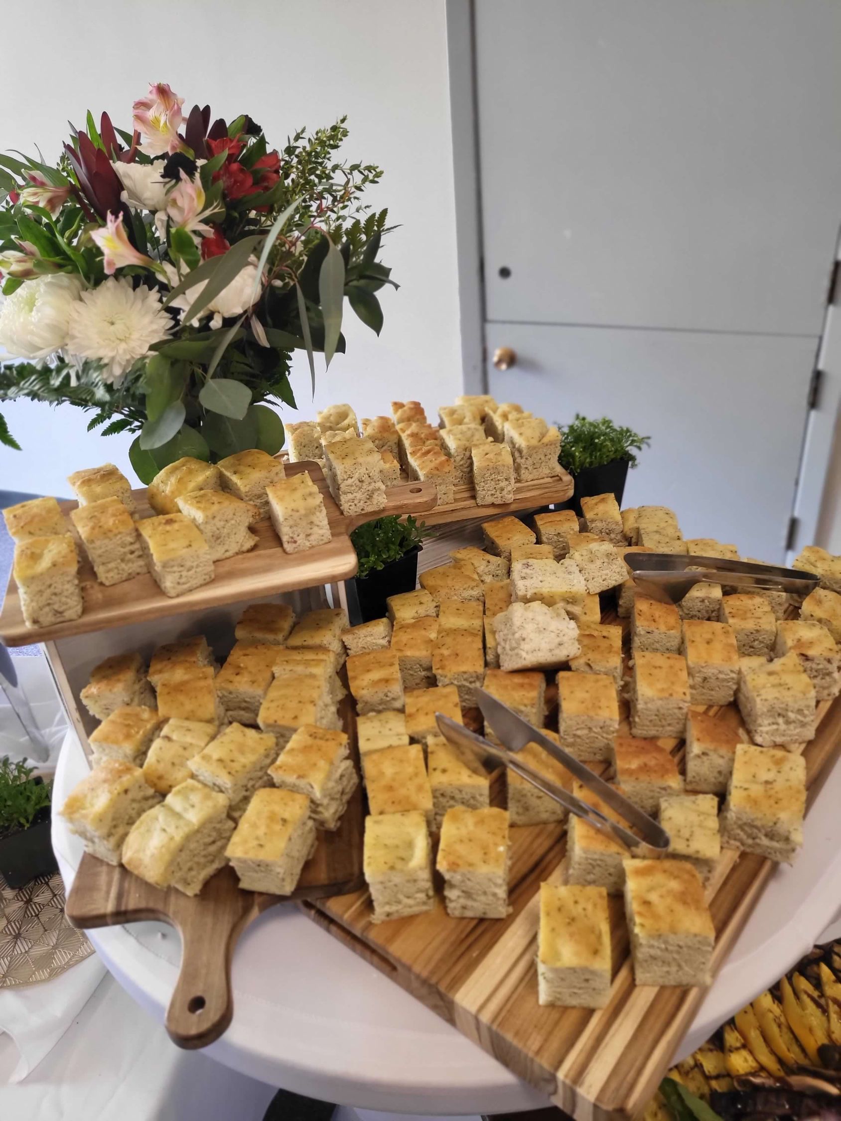 Focaccia bread squares arranged on wooden boards, a floral arrangement in the background.