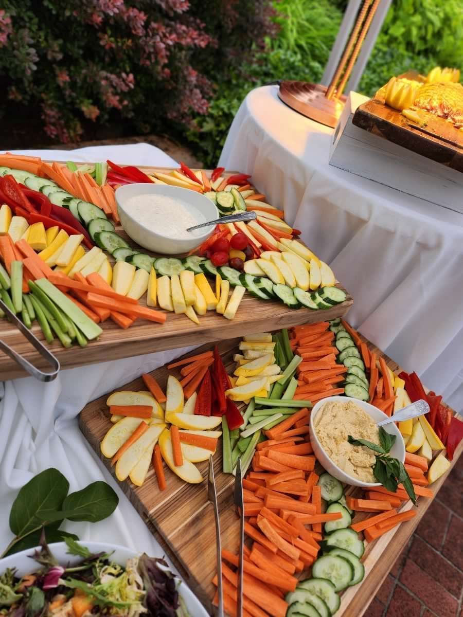 Two wooden platters of colorful vegetable crudités and dips on a table outdoors.