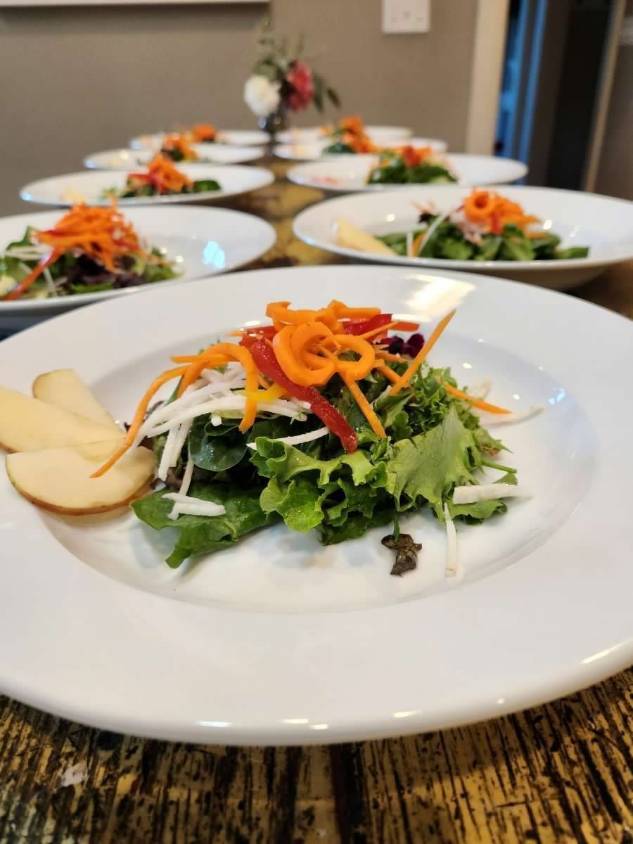 Plates of salad with carrots, greens, and apple slices, set on a wood table.