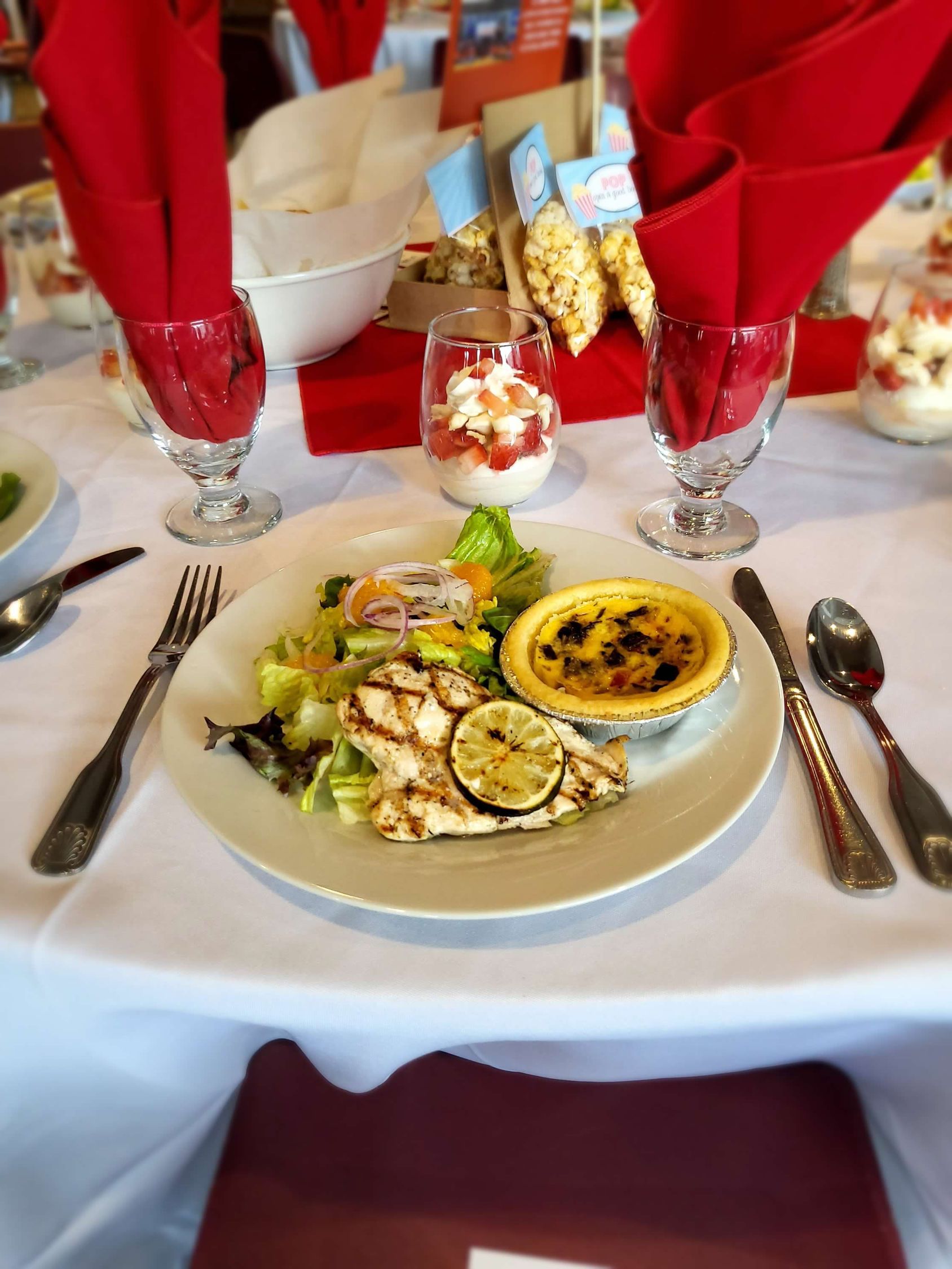 White plate with grilled chicken, salad, and tart on a table setting with red napkins.