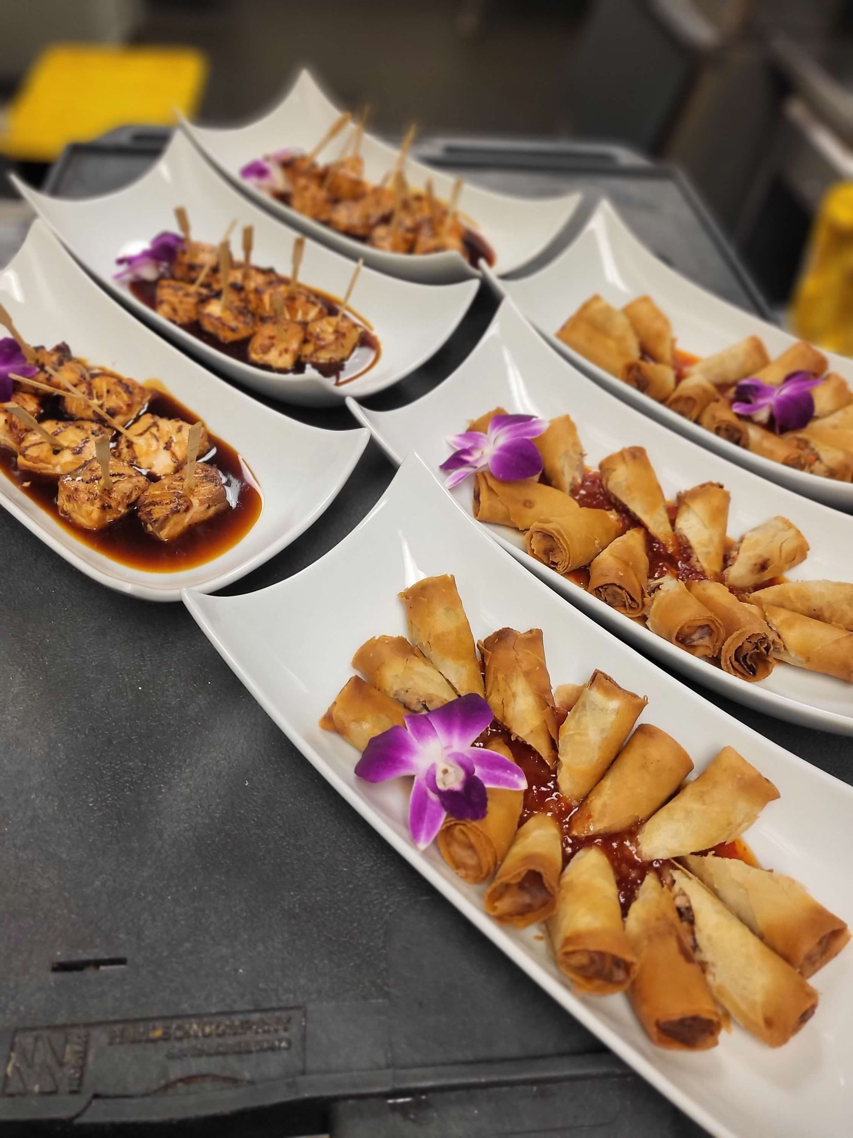 Platters of appetizers: spring rolls, skewers, and shrimp with flowers on a table.