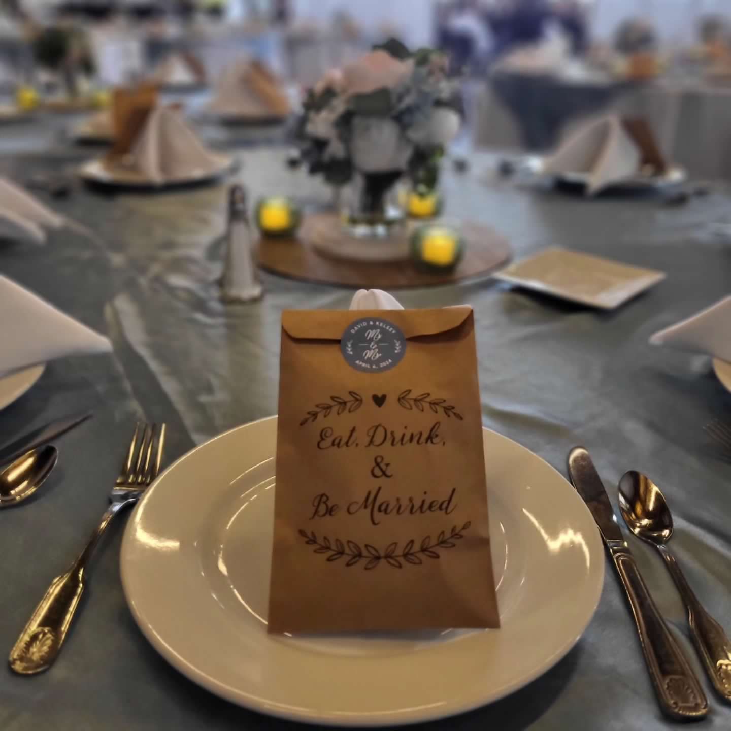 Wedding table setting with favor bag on a plate; blue tablecloth, silverware, and centerpiece visible.