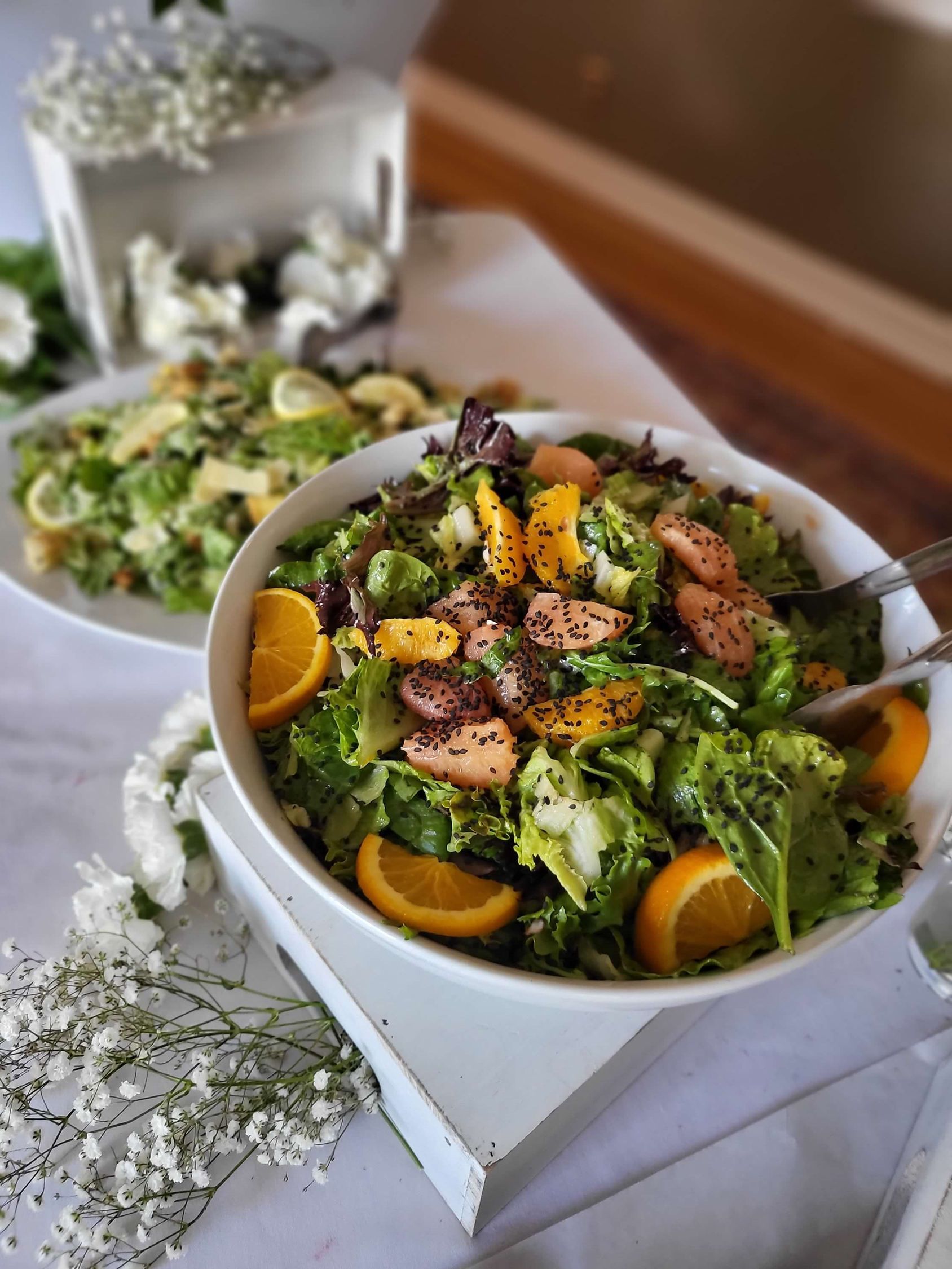 Two salads: one with oranges, lettuce, and dressing in a white bowl; other with croutons.