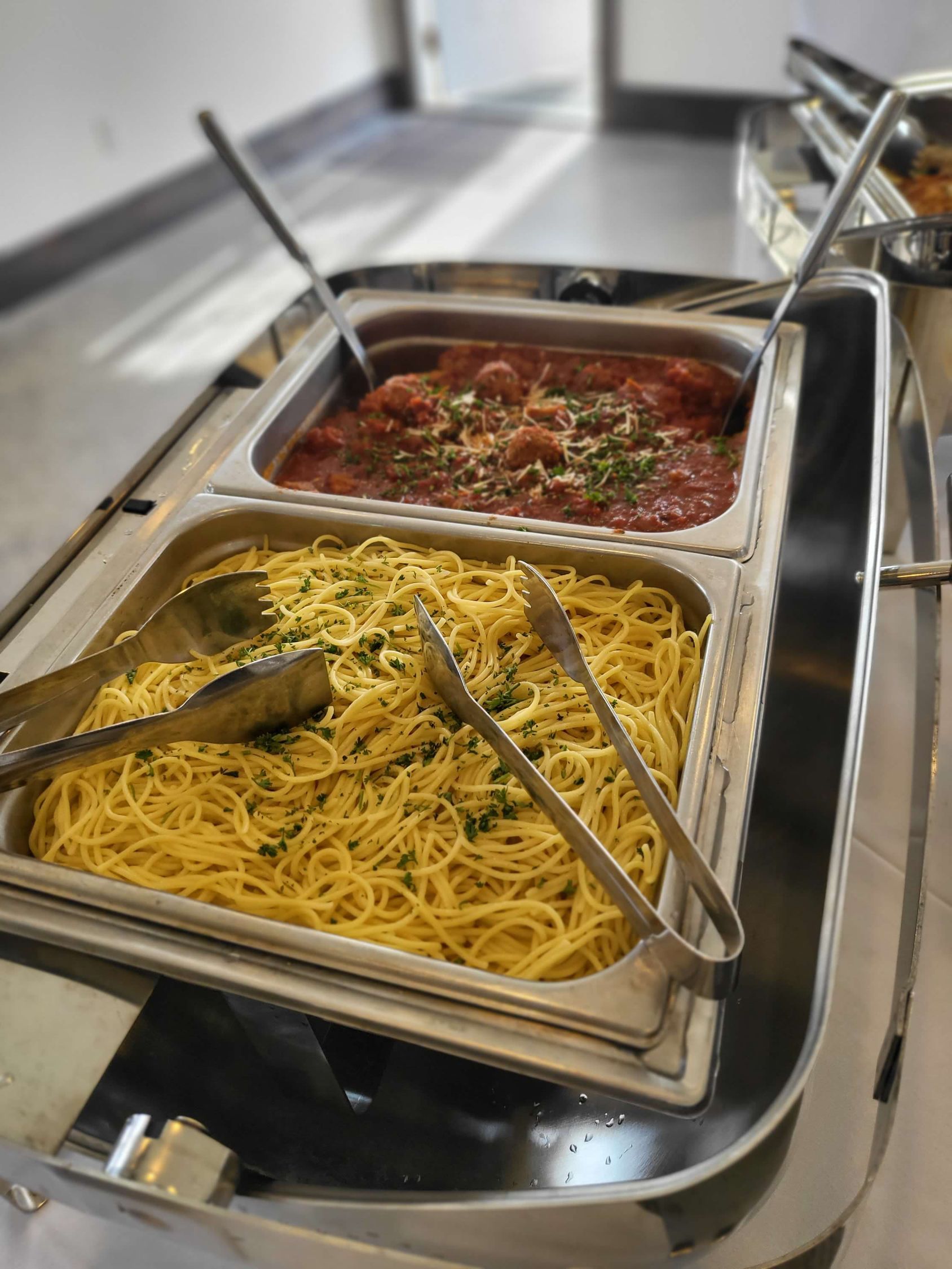 Pasta buffet with spaghetti and meatballs in a metal chafing dish.