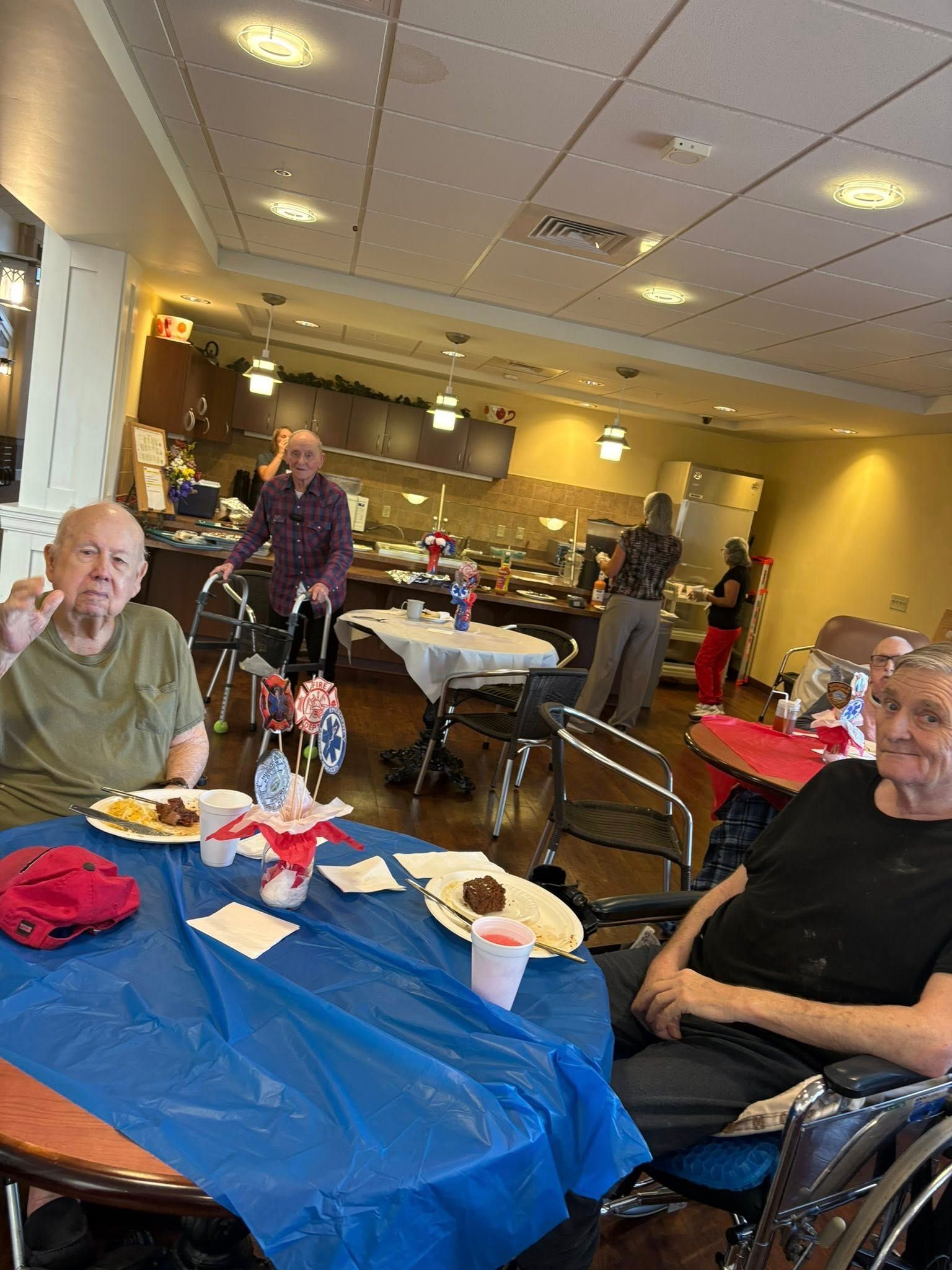 People at tables with food, celebrating in a community room. Some use walkers or wheelchairs.