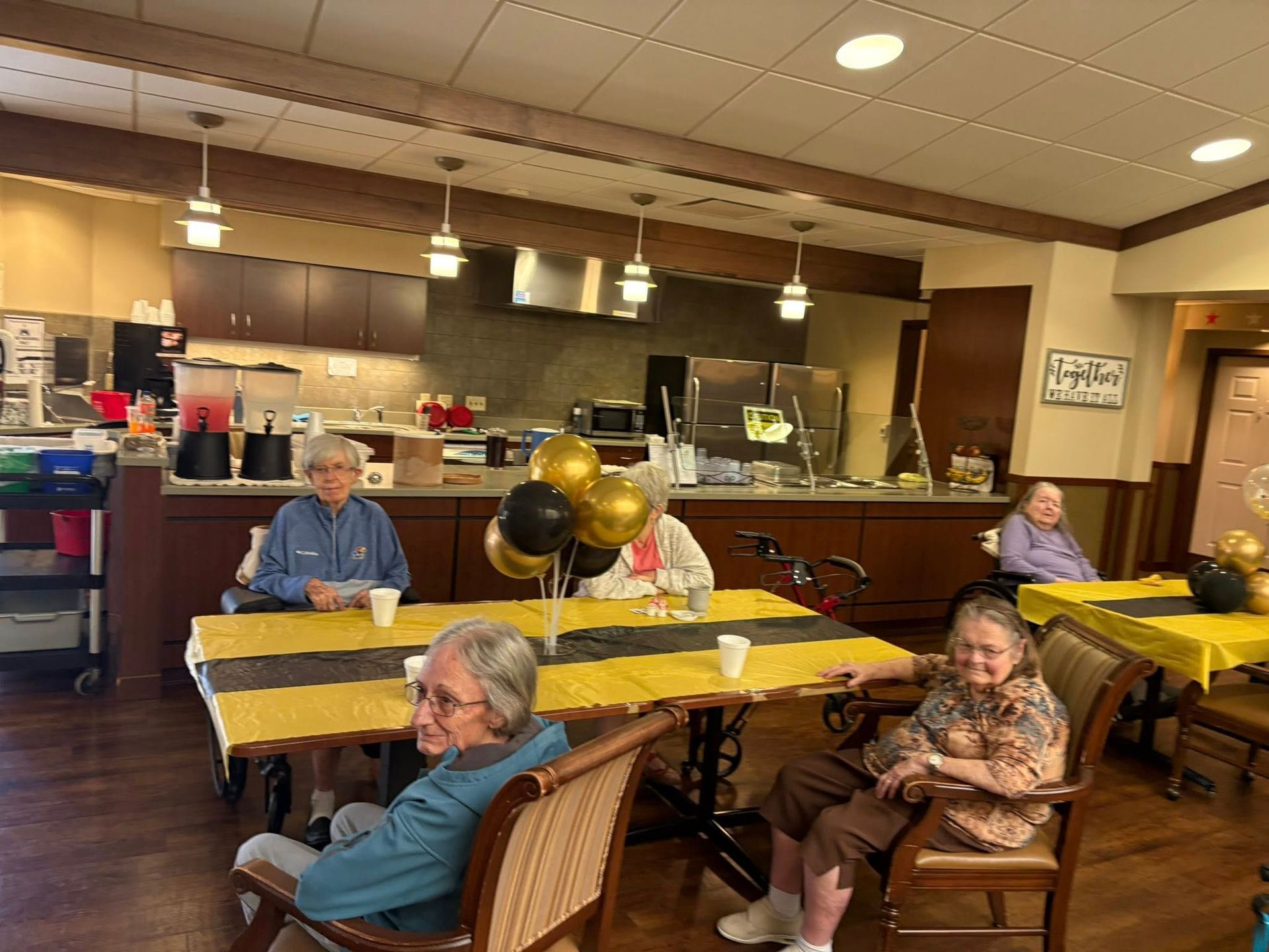 Seniors at a table in a room decorated with black and gold balloons, possibly a celebration.