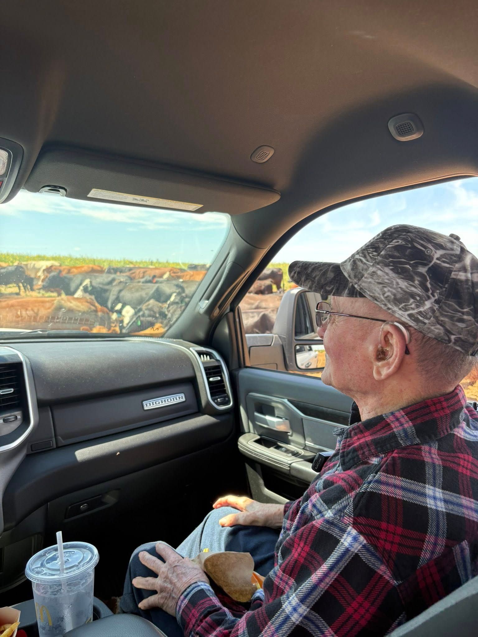 Man in a camo hat and plaid shirt looks out car window at a scenic view.